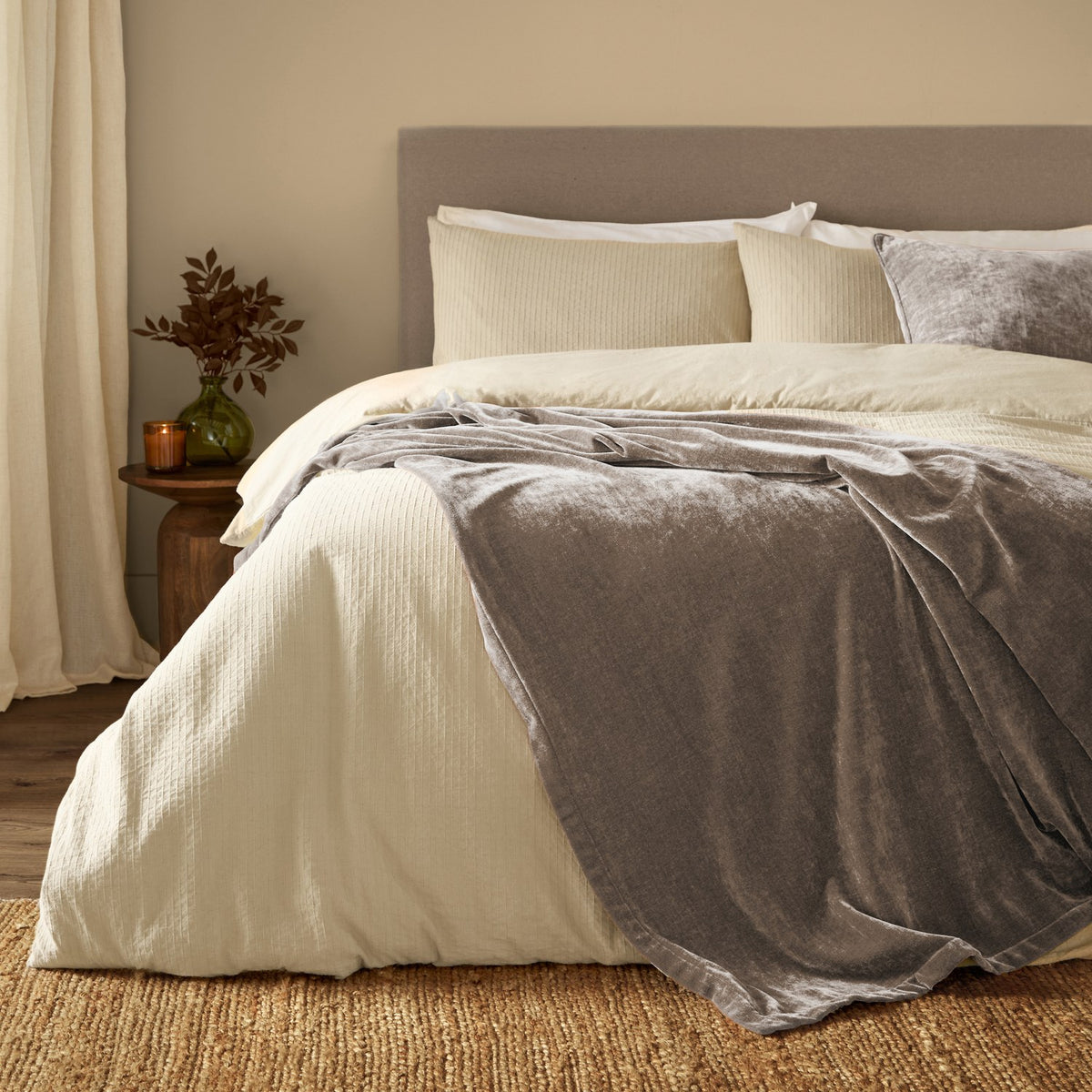 Heavy Chenille Eyelet Velvet Throw in greige draped over a cream bed with matching duvet and cushions in a bedroom setting.