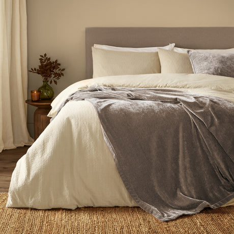 Heavy Chenille Eyelet Velvet Throw in greige draped over a cream bed with matching duvet and cushions in a bedroom setting.