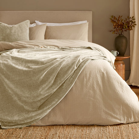 Heavy Chenille Eyelet Linen Throw in beige, draped over a bed with textured cream bedding, layered pillows, and a warm-toned bedroom setting.