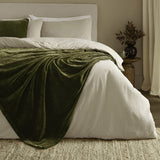 Heavy Chenille Eyelet Velvet Throw in olive green draped over a white bed with cream bedding, showing its dense pile and folds in a bedroom setting.