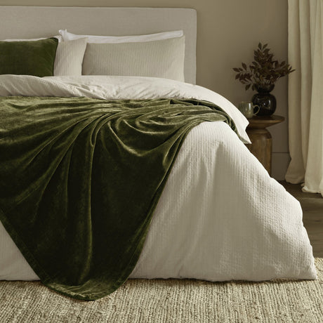 Heavy Chenille Eyelet Velvet Throw in olive green draped over a white bed with cream bedding, showing its dense pile and folds in a bedroom setting.