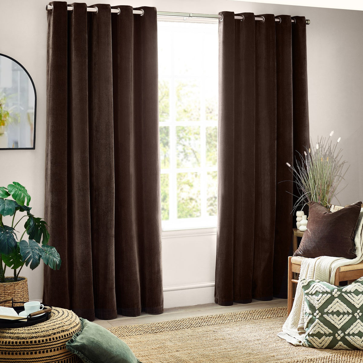 Heavy chenille velvet eyelet curtains in brown, hung floor-length with grommet top and clean vertical folds in a living room beside a large window.