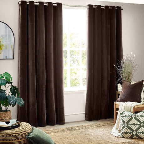 Heavy chenille velvet eyelet curtains in brown, hung floor-length with grommet top and clean vertical folds in a living room beside a large window.