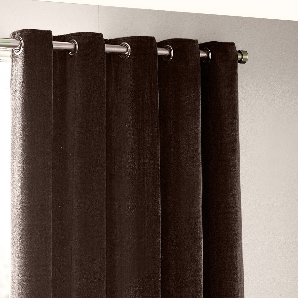 Brown heavy chenille velvet eyelet curtain panels with silver grommets, shown hanging in soft vertical folds from a metal curtain rod.