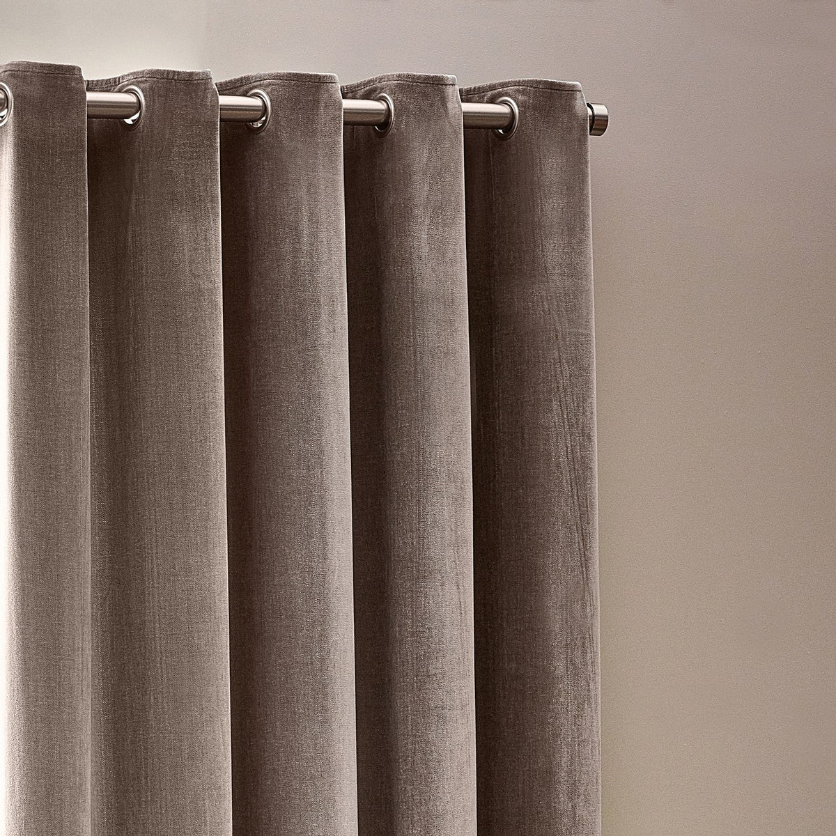 Heavy chenille velvet eyelet curtains in greige, shown hanging in soft folds on a brushed metal rod with visible eyelet grommets against a plain neutral wall.