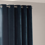 Heavy chenille velvet eyelet curtains in navy blue, hung on a chrome pole with metal grommets, falling in full rounded folds against a light wall.