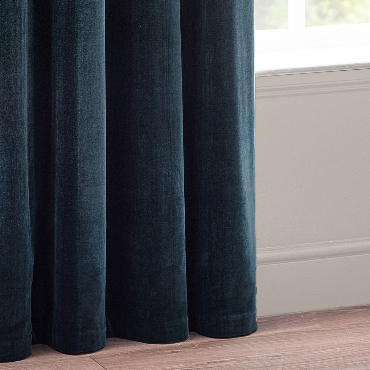 Heavy chenille velvet eyelet curtains in navy blue, shown pooling in full rounded folds beside a window with white sill and wood flooring.