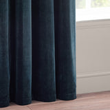 Heavy chenille velvet eyelet curtains in navy blue, shown pooling in full rounded folds beside a window with white sill and wood flooring.