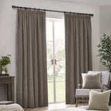 Heavy Chenille Plain Velvet Pencil Pleat Curtains in greige, shown hanging by a French door in a living room with an armchair and cushions nearby.