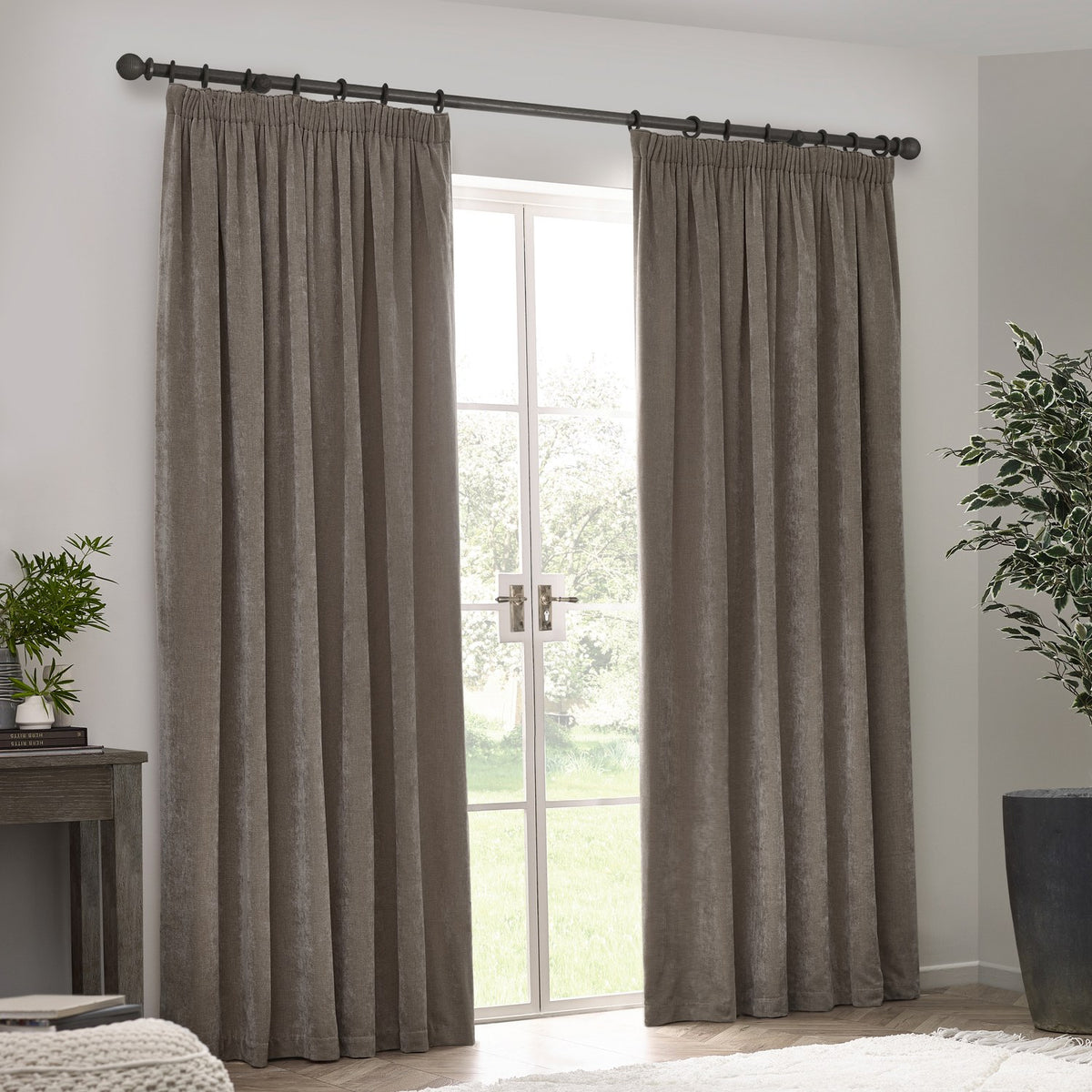Heavy chenille velvet pencil pleat curtains in greige, hung either side of a French door on a black rod, shown in a light neutral living room setting.