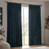 Navy velvet pencil pleat curtains with pencil pleat heading on a wooden pole, hung either side of a window in a living room setting.