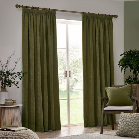 Heavy chenille pencil pleat curtains in olive green, shown floor-length either side of a French door in a living room with a matching cushion, wooden chair, and potted plant.