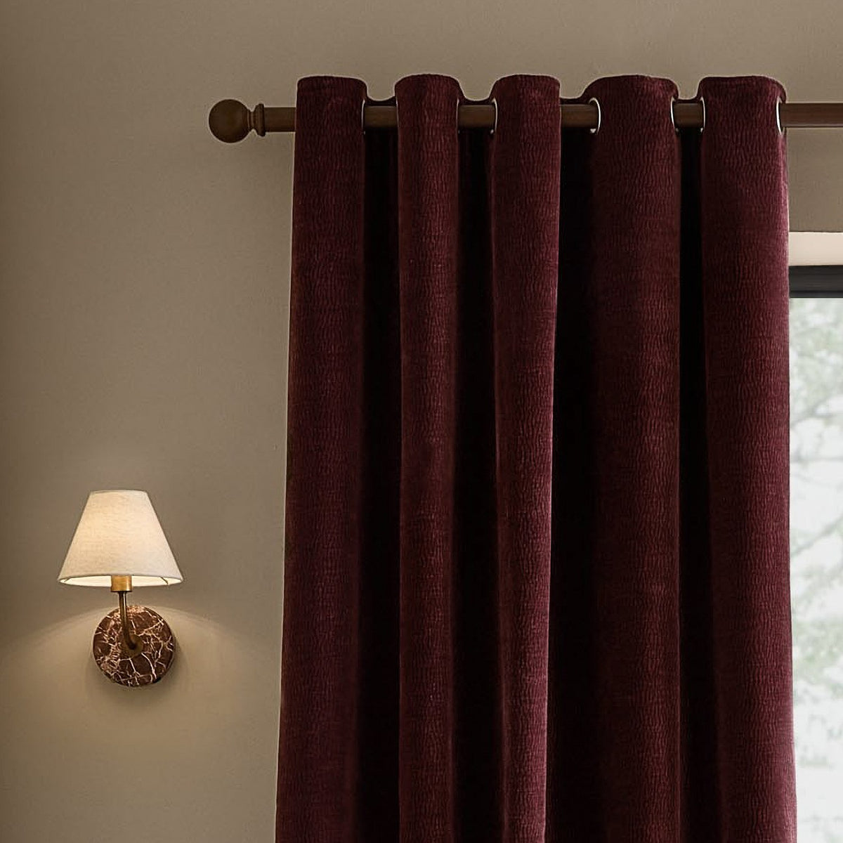 Heath Washed Velvet Fully Lined Eyelet Curtains in Beetroot, textured dark red fabric with metal eyelets on a wooden pole, shown hanging beside a window in a living room.