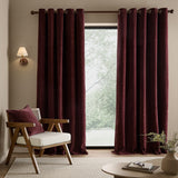 Heath Washed Velvet Fully Lined Eyelet Curtains in beetroot, shown hanging floor-length beside a window in a living room with a wooden armchair and cream cushion.