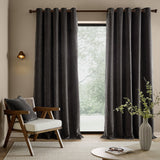 Heath Washed Velvet Fully Lined Eyelet Curtains in charcoal, shown in a living room with grommet top on a dark metal pole, framing a glass door beside a wooden armchair.