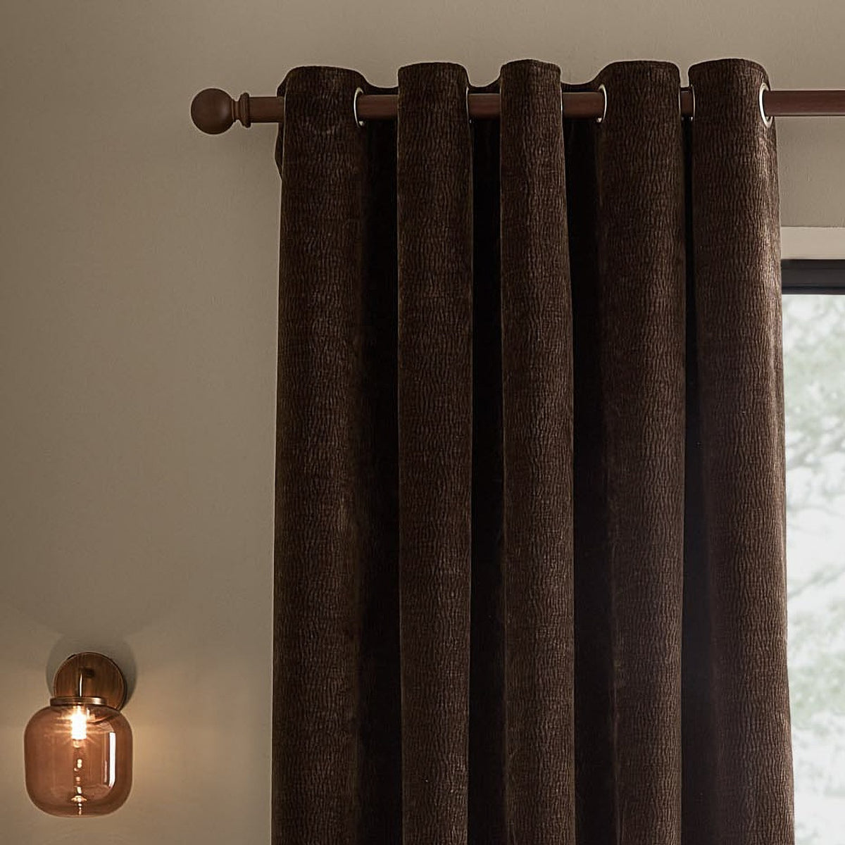 Heath eyelet curtains in espresso brown washed velvet with jacquard texture, shown on a dark wooden pole with round finials against a neutral wall.