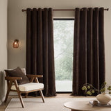 Heath Washed Velvet Fully Lined Eyelet Curtains in espresso brown hanging on a metal pole either side of a glass door in a living room with an armchair and side table.