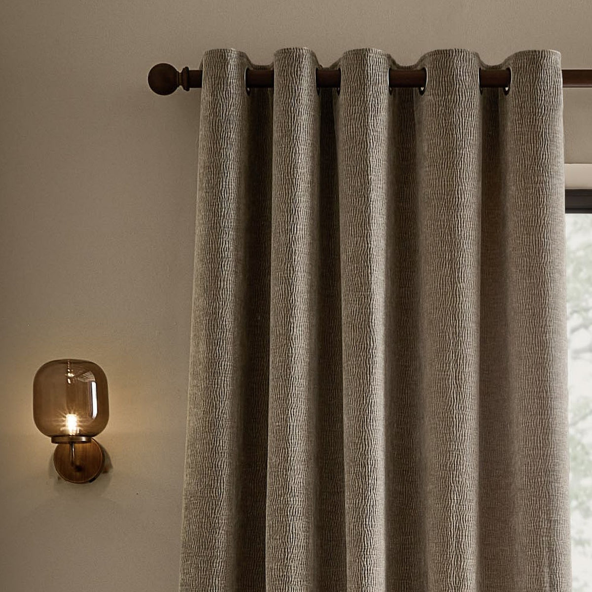 Heath Washed Velvet Jacquard Fully Lined Eyelet Curtains in greige, textured fabric on a dark eyelet rod, styled in a living room beside a wall-mounted lamp.