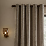Heath Washed Velvet Jacquard Fully Lined Eyelet Curtains in greige, textured fabric on a dark eyelet rod, styled in a living room beside a wall-mounted lamp.