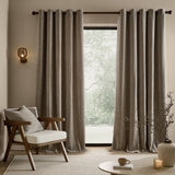 Heath Washed Velvet Jacquard Fully Lined Eyelet Curtains in greige, hung on a dark rod beside a window in a living room with a wooden armchair.