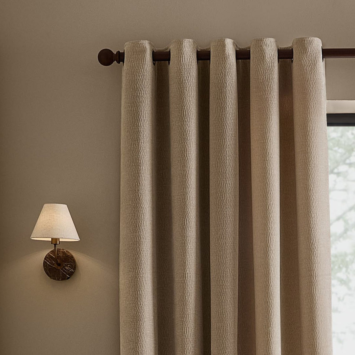 Heath eyelet curtains in beige washed velvet with textured jacquard weave, hung on a dark rod beside a wall lamp in a neutral-toned room.