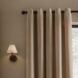 Heath eyelet curtains in beige washed velvet with textured jacquard weave, hung on a dark rod beside a wall lamp in a neutral-toned room.
