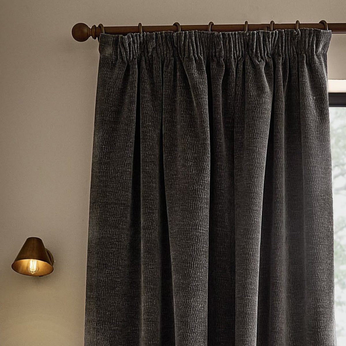 Heath Washed Velvet Pencil Pleat Curtains in charcoal grey, shown hung on a bronze pole with pencil pleat heading, textured pile visible in a living room setting.