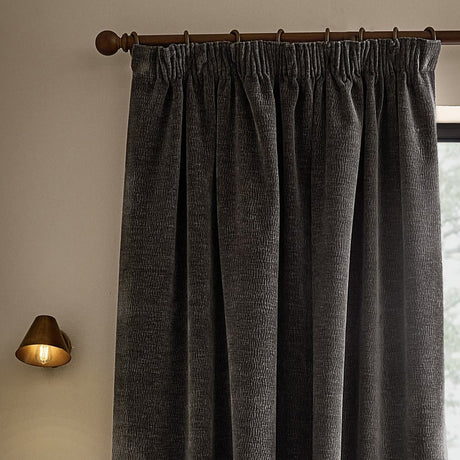 Heath Washed Velvet Pencil Pleat Curtains in charcoal grey, shown hung on a bronze pole with pencil pleat heading, textured pile visible in a living room setting.