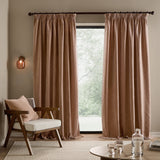 Heath Washed Velvet Pencil Pleat Curtains in Cotta, a pair of terracotta-pink pencil pleat panels shown pooling by a window in a living room with an armchair.