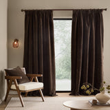 Heath washed velvet pencil pleat curtains in espresso brown, hung on a rod either side of a window in a living room with an armchair and side table.