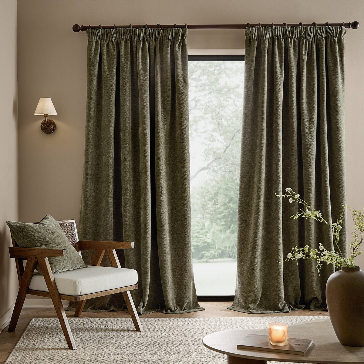 Heath washed velvet pencil pleat curtains in Eucalyptus green, pencil-pleat heading on a dark pole, shown floor-length beside a glazed door in a living room.