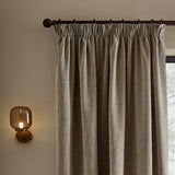 Heath washed velvet pencil pleat curtains in greige, hung on a dark rod with pencil pleat heading, shown beside a window in a softly lit room with a wall-mounted glass sconce.