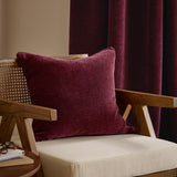 Heath Washed Velvet Jacquard Polyester Cushion in beetroot red, textured square design on a wooden armchair with cane detailing and burgundy curtains behind.