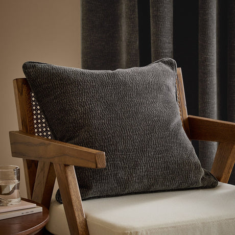 Heath washed velvet jacquard cushion in charcoal, square 50x50cm with a textured woven surface, shown on a wooden armchair in a living room setting.
