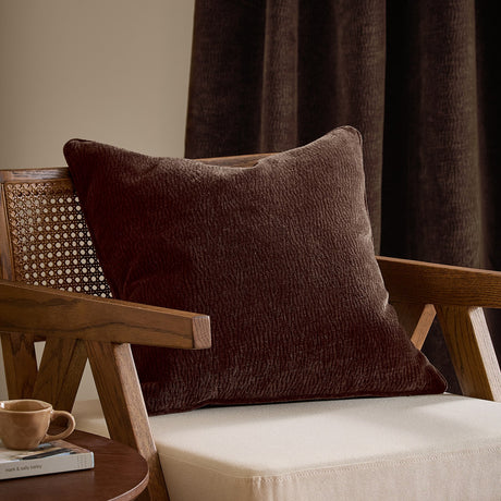 Heath Washed Velvet Jacquard Polyester Cushion in espresso brown, square with a textured pile, styled on a wooden armchair with cream upholstery.