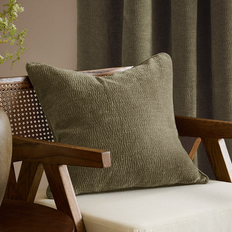 Heath Washed Velvet Jacquard Polyester Cushion in eucalyptus green with textured pile, shown on a wooden armchair in a living room setting.