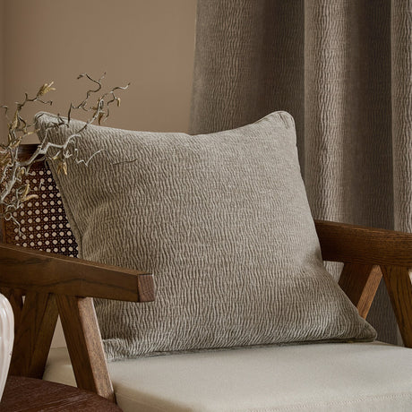 Heath Washed Velvet Jacquard Polyester Cushion in greige with rippled pile texture, styled on a wooden armchair in a living room setting.
