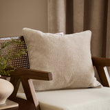 Heath Washed Velvet Jacquard Linen Cushion in cream, square with piped edges and rippling textured surface, styled on a wooden armchair in a living room.