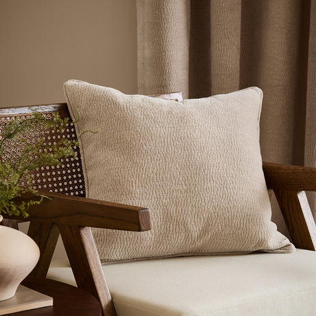 Heath Washed Velvet Jacquard Linen Cushion in cream, square with piped edges and rippling textured surface, styled on a wooden armchair in a living room.