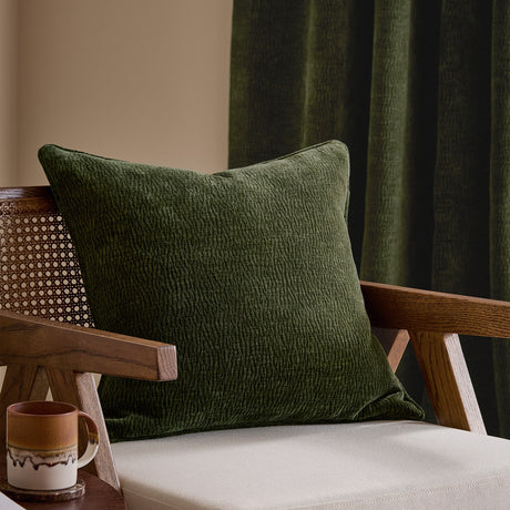 Heath Washed Velvet Jacquard Polyester Cushion in olive green, 50x50cm square with textured woven finish, styled on a wooden armchair in a living room.