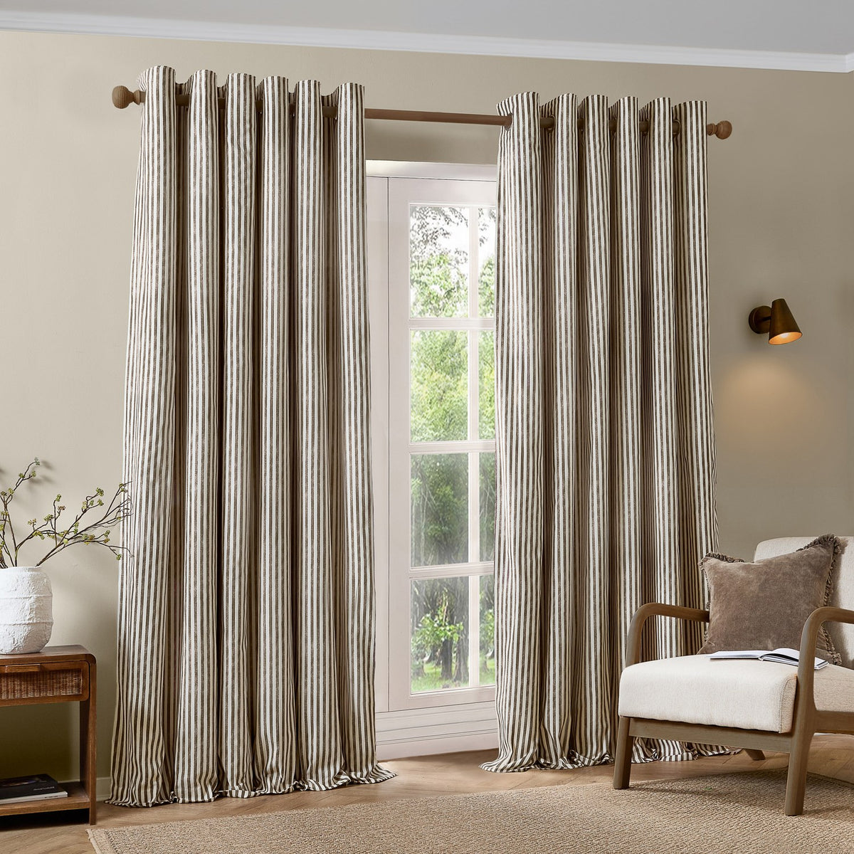 Hebden Cotton Fully Lined Eyelet Curtains in chocolate brown and cream vertical stripe, shown hanging on a wooden pole in a living room window setting.