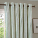Hebden Cotton Fully Lined Eyelet Curtain in Eucalyptus, green and cream vertical stripe fabric with eyelet heading on a wooden pole, shown in a living room setting.