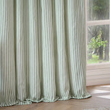 Hebden Cotton Fully Lined Eyelet Curtains in Eucalyptus, showing draped folds of green and white vertical stripe fabric hanging beside a window in a living room.