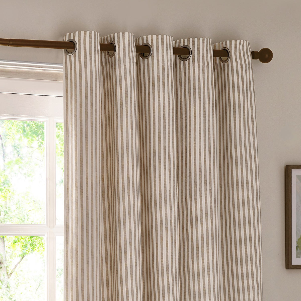 Hebden cotton eyelet curtain in natural beige and white vertical stripe, hung on a wooden pole with metal eyelets in a living room window setting.