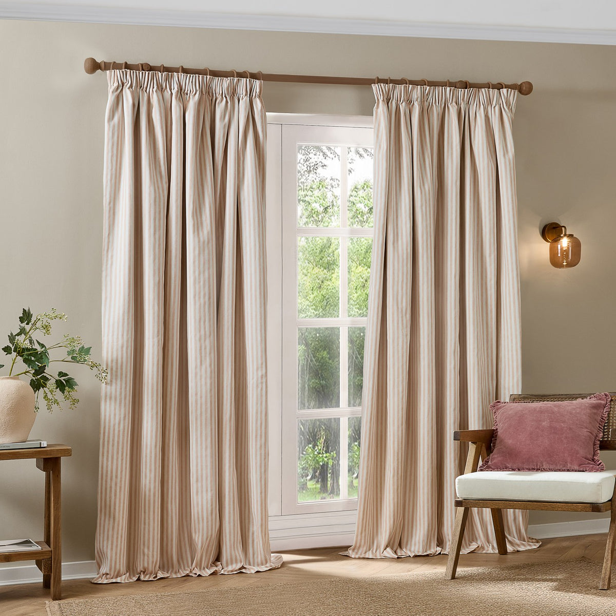 Hebden fully lined pencil pleat curtains in blush and cream stripe cotton, shown pinch-pleated on a wooden pole in a living room beside a window.