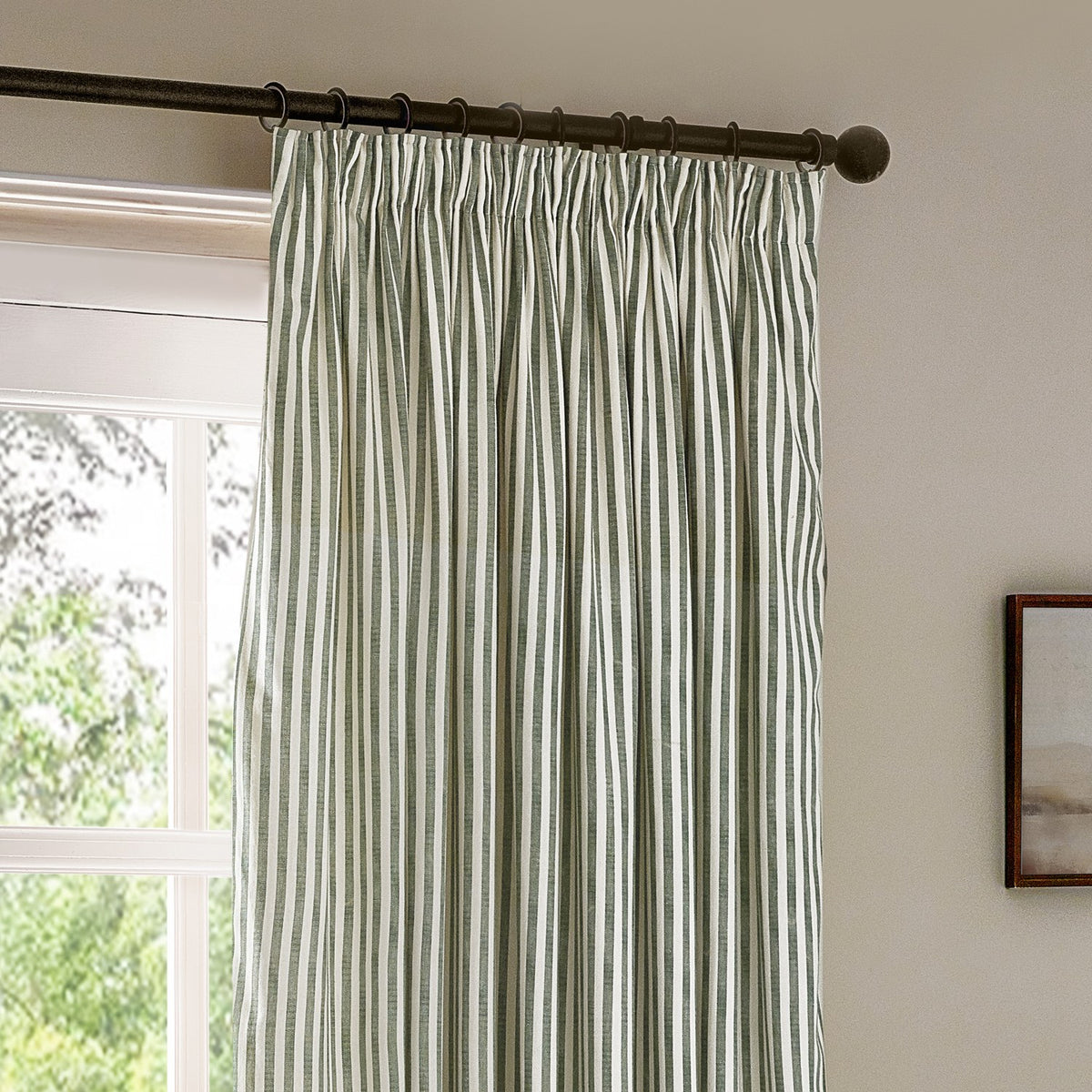 Hebden Striped Cotton Pencil Pleat Curtains in forest green, pinch-pleat heading on a dark rod, hung at a window in a neutral-toned room.