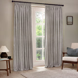 Hebden Striped Cotton Pencil Pleat Curtains in grey and white, hung on a black pole beside a window in a living room with an armchair and side table.