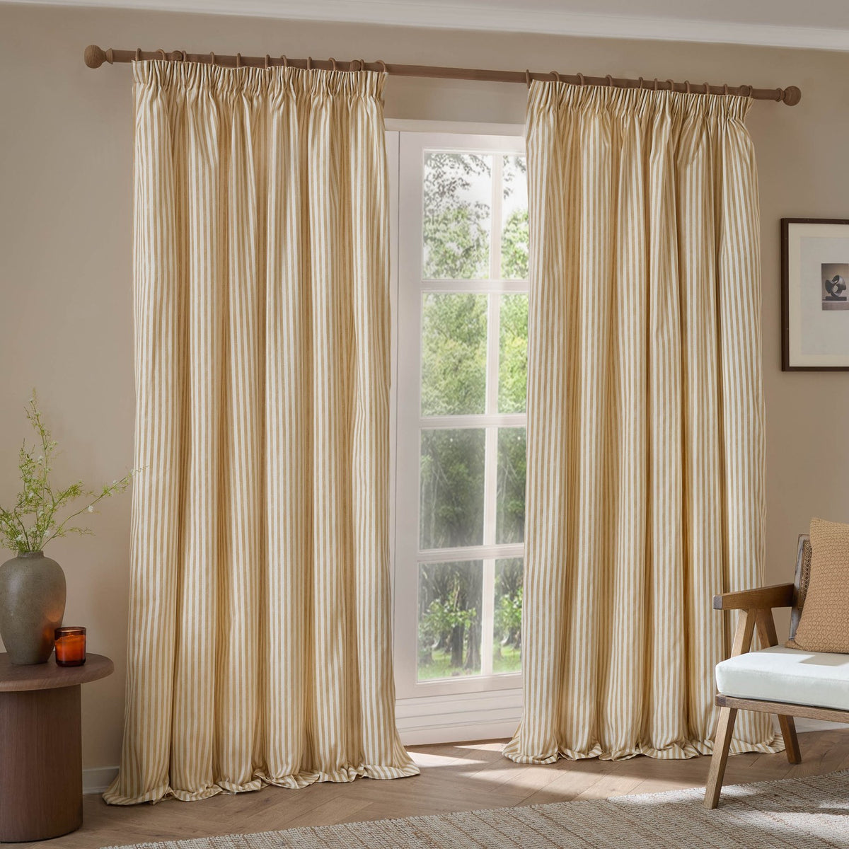 Hebden fully lined pencil pleat curtains in honey-yellow and cream cotton stripe, hung on a wooden pole beside a window in a living room.