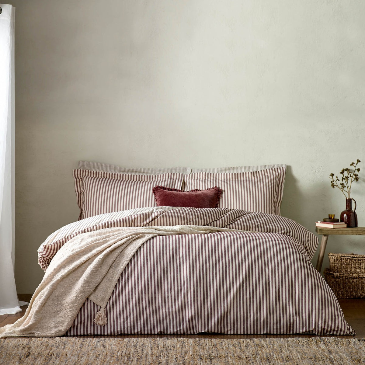 Hebden Cotton Melange Duvet Cover Set in Beetroot, showing beetroot-and-cream striped bedding with matching pillowcases and a beetroot cushion on a bed in a neutral bedroom setting.