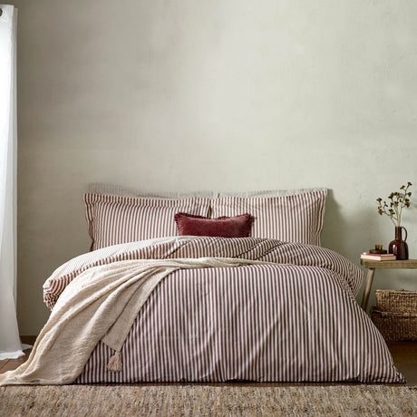 Hebden Cotton Melange Duvet Cover Set in Beetroot, showing beetroot-and-cream striped bedding with matching pillowcases and a beetroot cushion on a bed in a neutral bedroom setting.